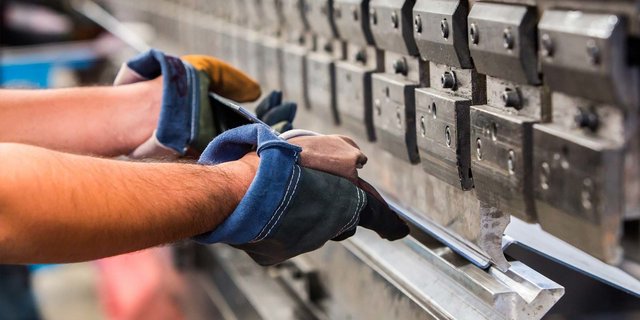 Ein Arbeiter mit Handschuhen hält ein Metallstück, während er eine präzise Bearbeitung an einer Maschine vornimmt.