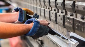 Ein Arbeiter mit Handschuhen hält ein Metallstück, während er eine präzise Bearbeitung an einer Maschine vornimmt.